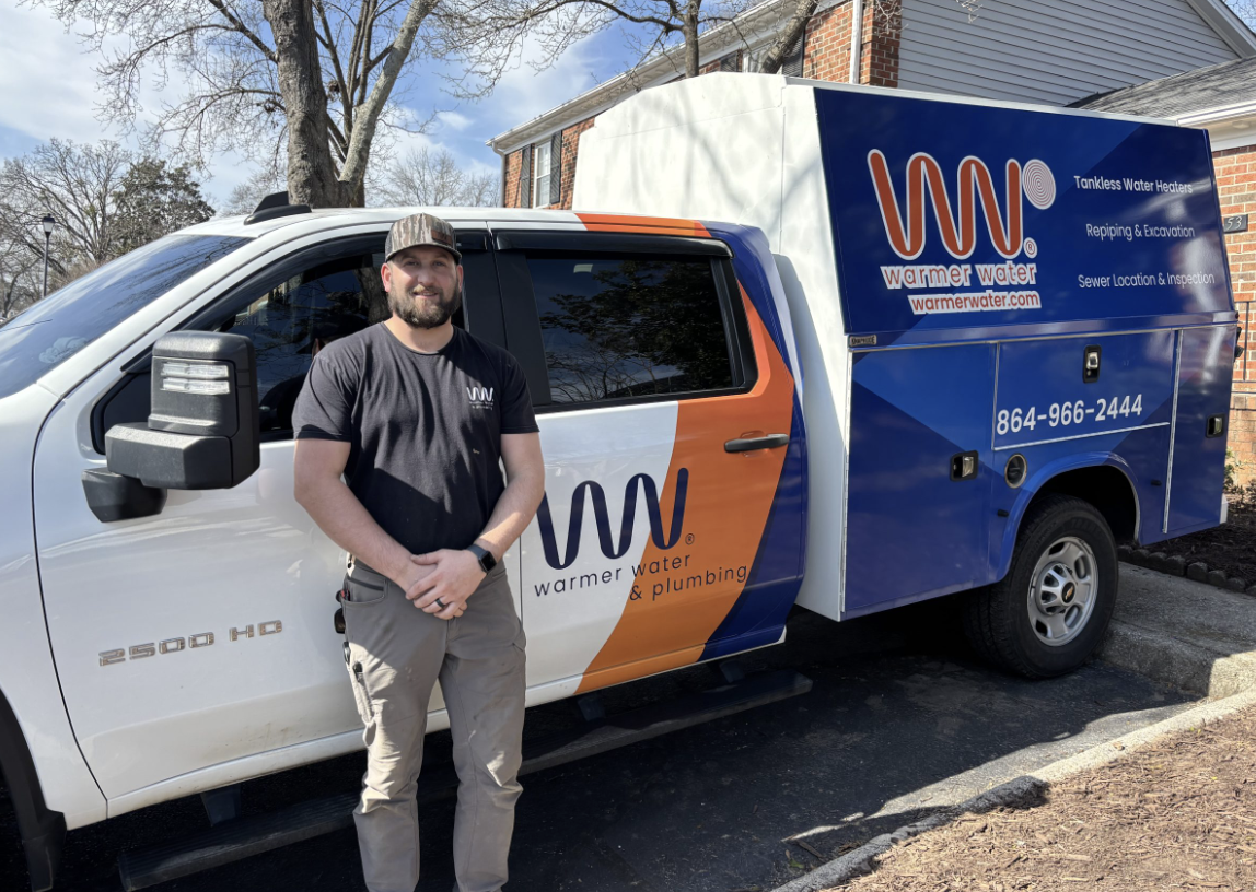 Josh Tackett of Warmer Water and Plumbing in front of a branded service truck
